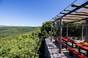 A scenic outdoor seating area with stone walls and wooden benches, overlooking a lush valley.