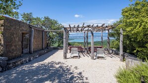 Een rustieke buitenruimte met een pergola, stenen muren en uitzicht op een meer.