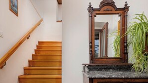 Een houten trap met een leuning, een houten dressoir met lades, een spiegel en een lijst met een afbeelding aan de muur.