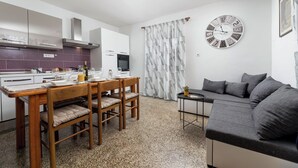 Een moderne keuken met witte kasten, een eettafel gedekt voor vier personen en een grijze bank in de woonkamer.