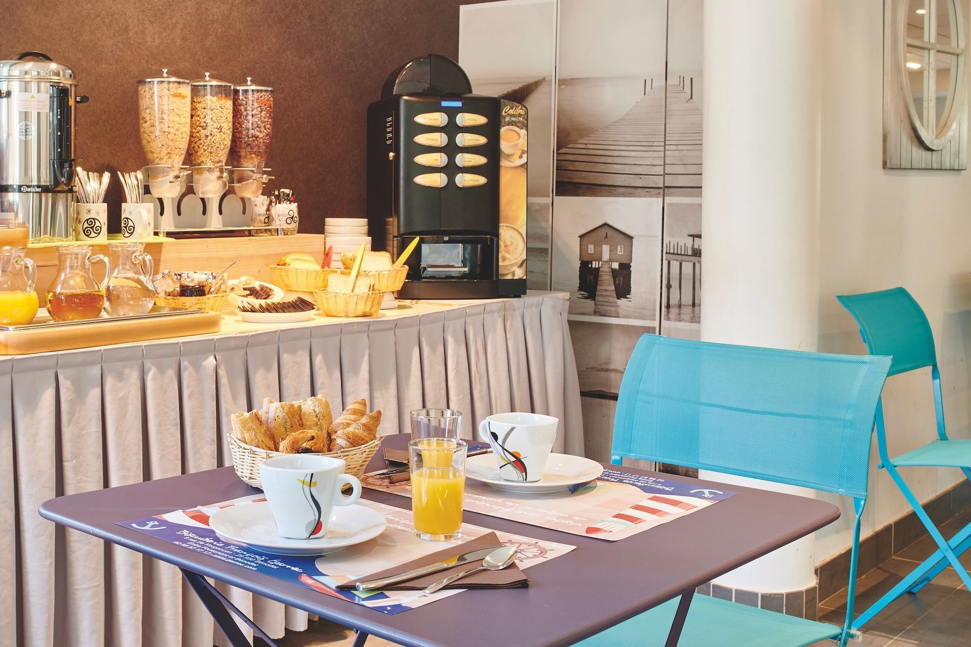 A breakfast bar with coffee machines, a selection of pastries, and a seating area with a chair and table.