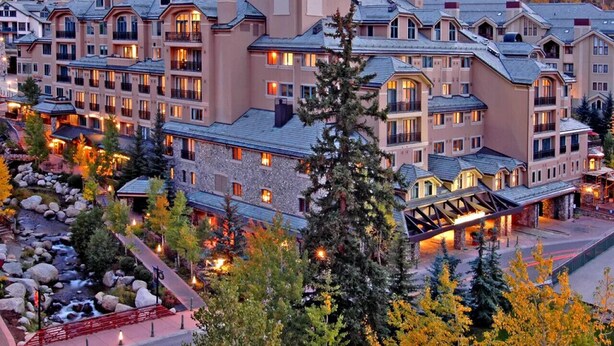 Un hotel a più piani con un cortile centrale, circondato da alberi e uno sfondo montuoso.