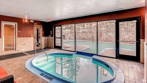 Una piscina interna con un cartello 'NO DIVING', una sauna e un muro in pietra con vista su un giardino.