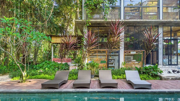 A pool area with lounge chairs and a building with a balcony. - Gunung An Retreat (Ubud)