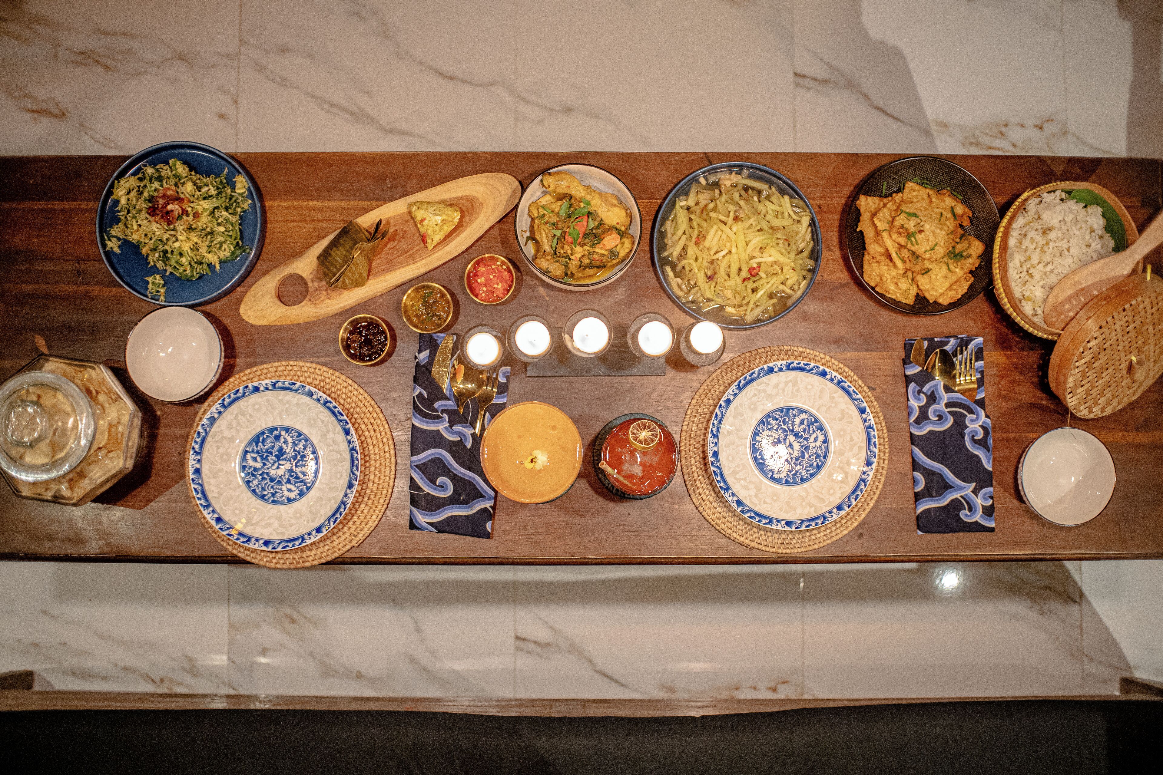 A wooden table with various dishes and condiments, including a bowl of salad, a plate of rice, and several small bowls with sauces.