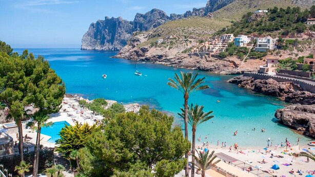 Une ville côtière bordée d’une mer d’un bleu éclatant, de falaises rocheuses et d’une plage aménagée avec des parasols et où se promènent des gens.