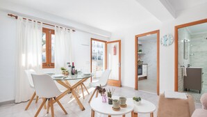 Un salon moderne avec un coin repas, une cuisine ouverte sur le salon par une porte, et une salle de bain dotée d’une douche en verre.
