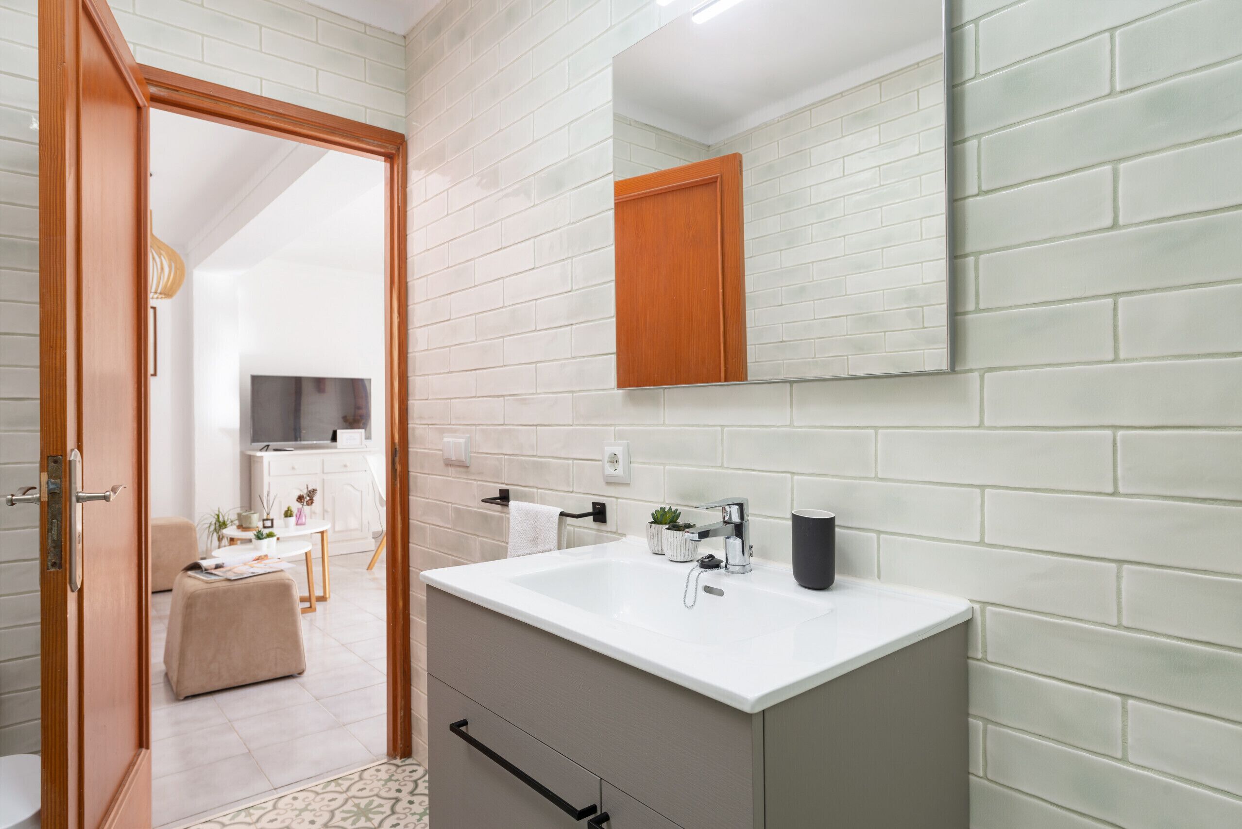 A modern bathroom with a white sink, a mirror, and a wooden cabinet.