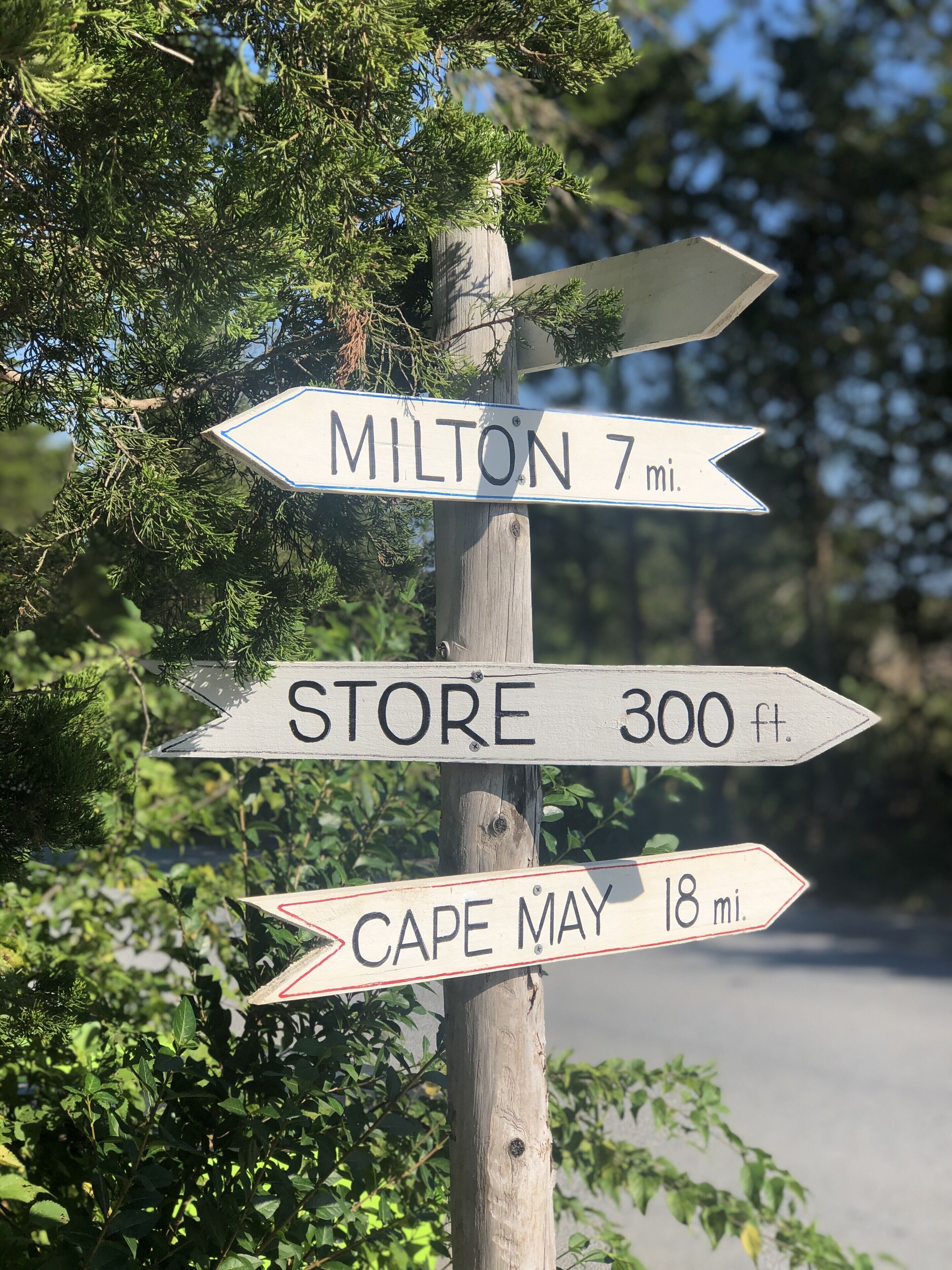 Un poste de señales direccionales con tres indicaciones: Milton, 7 millas; Tienda, 300 pies; y Cape May, 18 millas.