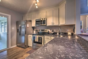 A modern kitchen with stainless steel appliances, white cabinetry, and a marble countertop.