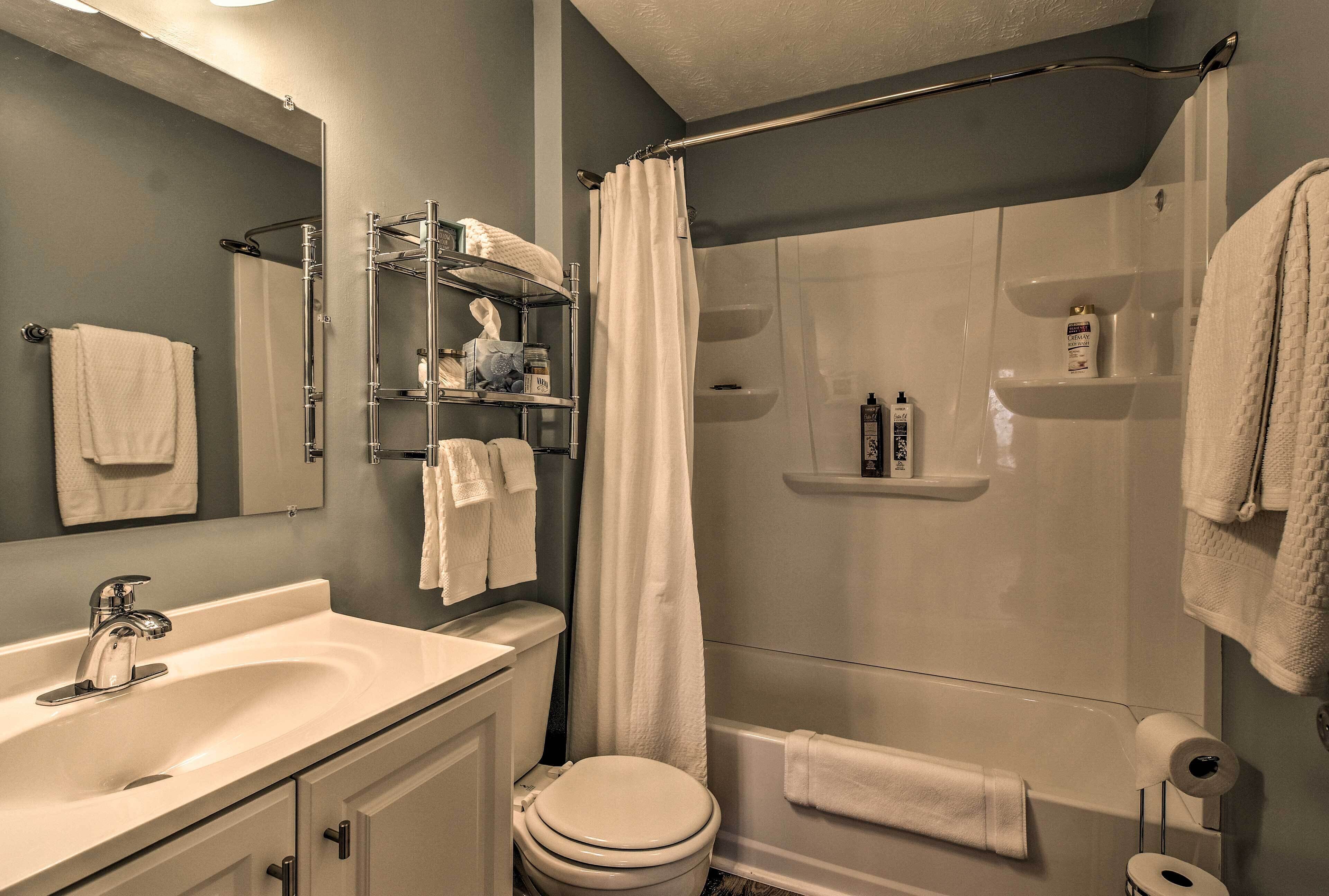 Een moderne badkamer met een wastafel, toilet, douche en planken met toiletartikelen.