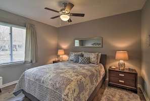 A bedroom with a bed, two bedside tables, a ceiling fan, a window with curtains, and a mirror on the wall.