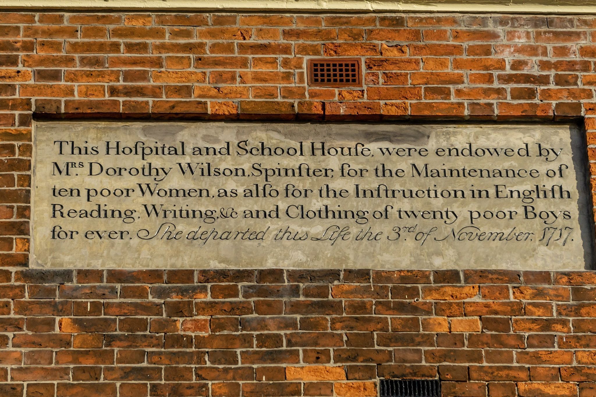 A brick wall with a plaque detailing a historical endowment for a hospital and school house.