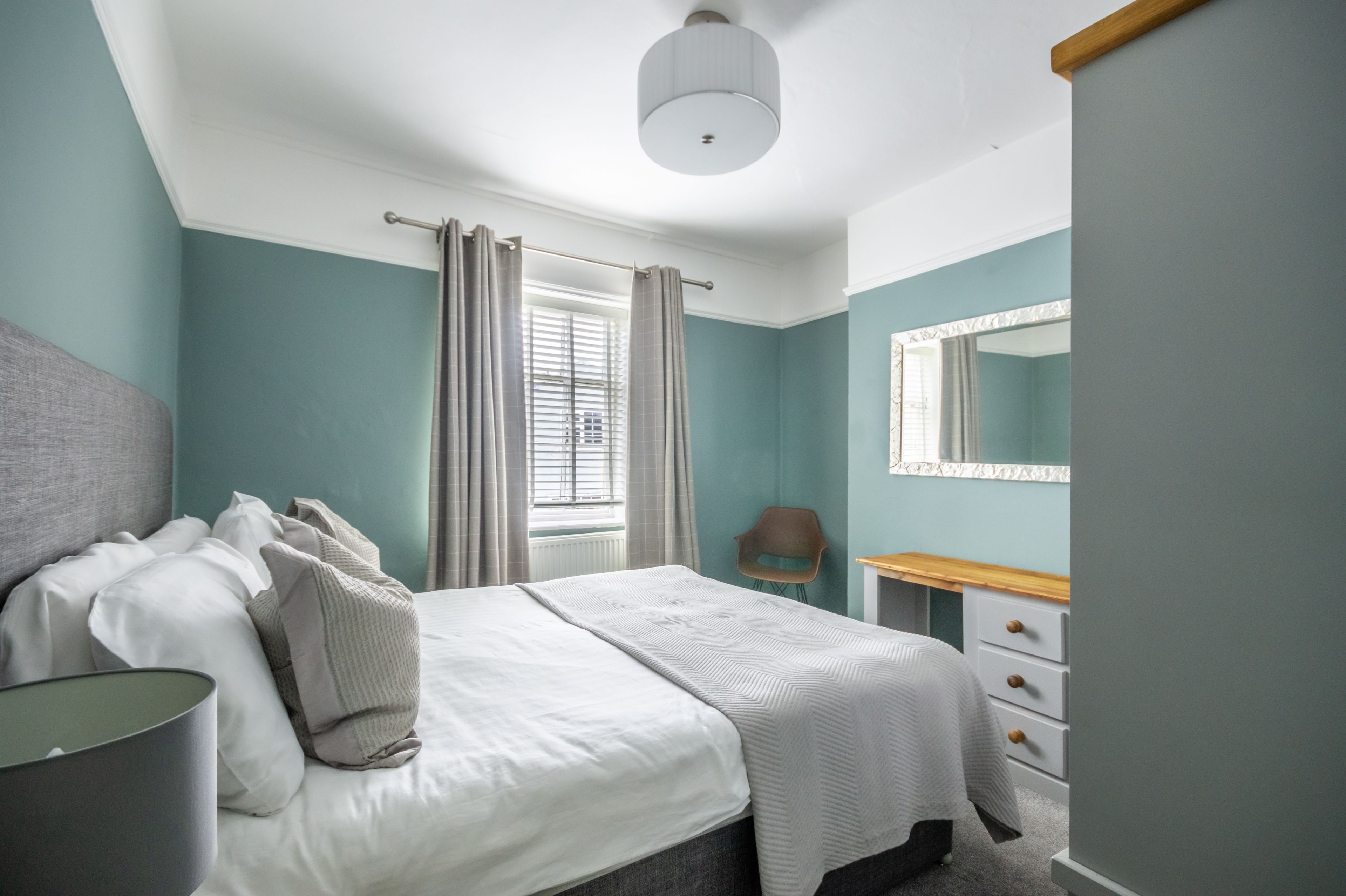 A bedroom with a bed, bedside table, chair, and a mirror.