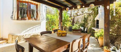 An outdoor patio with a wooden table and chairs, surrounded by potted plants and a stone wall.