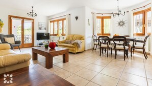 A spacious living room with a sofa, a coffee table, a TV, and a dining area with chairs and a table. - Villa MIMOSA by Abahana Villas (Benitachell)