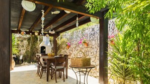 An outdoor patio with stone walls, a stone table, and wooden chairs. - Villa MIMOSA by Abahana Villas (Benitachell)