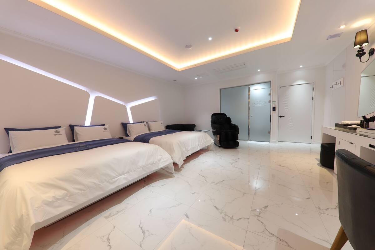 Ein modernes Hotelzimmer mit zwei Betten, einem Massagesessel, einem großen Spiegel und einem sauberen Boden mit Marmorplatten.