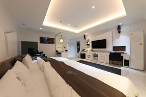 A modern hotel room with a large bed, a desk, a TV, and a seating area.