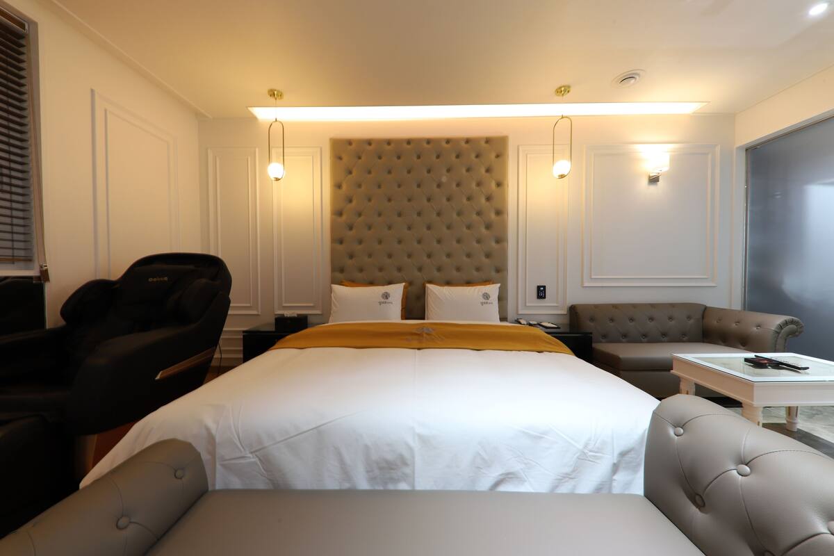 Ein Hotelzimmer mit einem großen Bett, zwei Sesseln, einem Sofa, einem Massagesessel und einem kleinen Tisch.