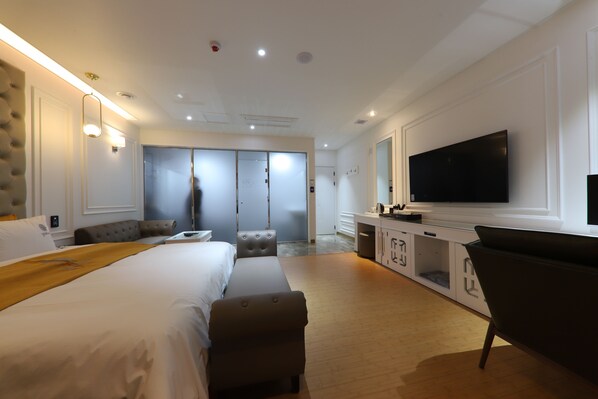 A modern hotel room with a large bed, a flat-screen TV, a desk, and a seating area.