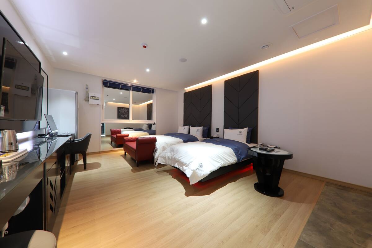 Ein modernes Hotelzimmer mit einer Küchenzeile, zwei Betten, einem roten Sofa und einem kleinen Tisch.