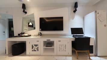 Una habitación de hotel moderna con una televisión de pantalla plana montada en la pared, un escritorio con una computadora portátil, una silla y un cubo de basura pequeño.