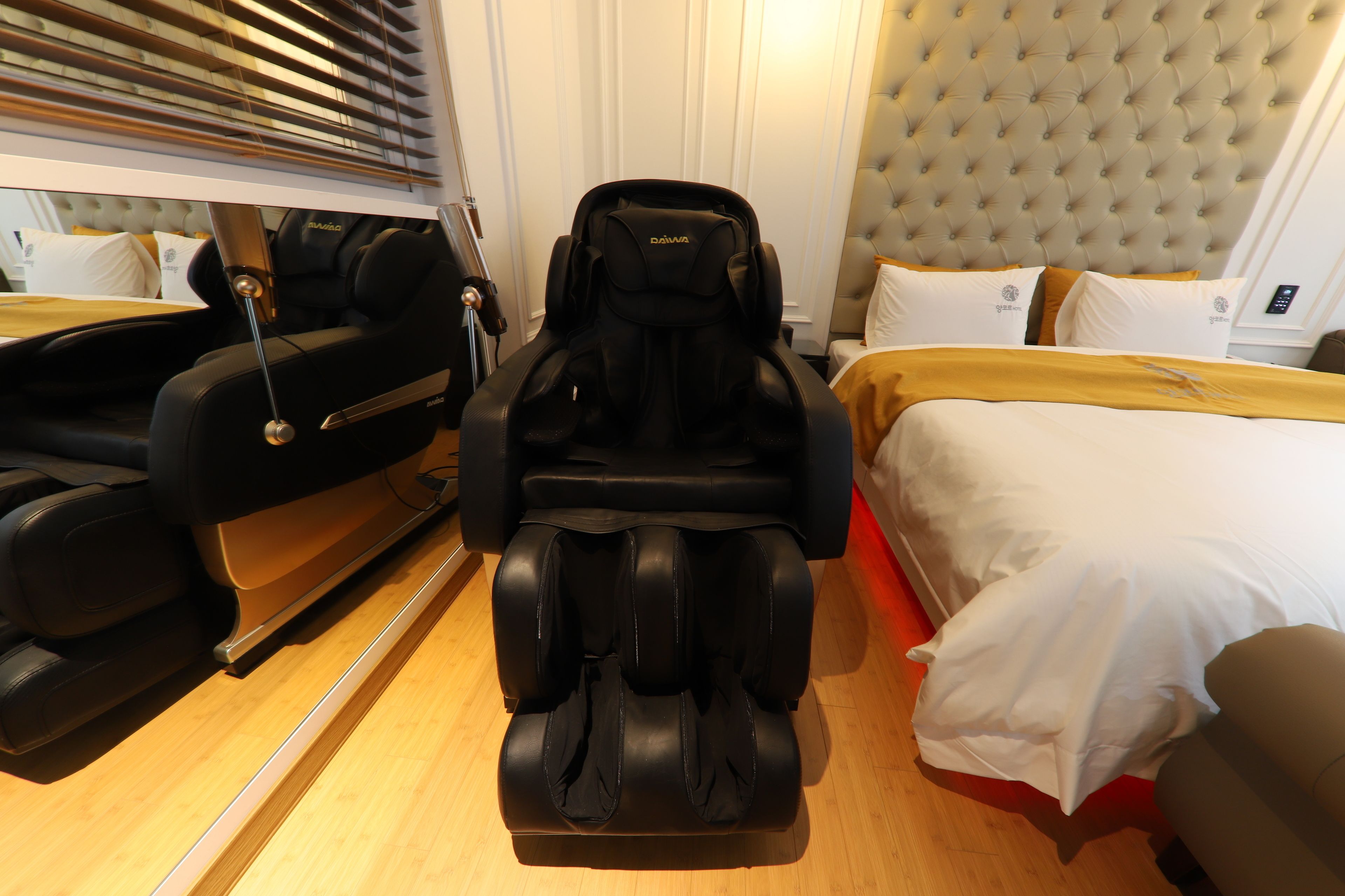 A massage chair in a hotel room with a bed, a bedside table, and a lamp.