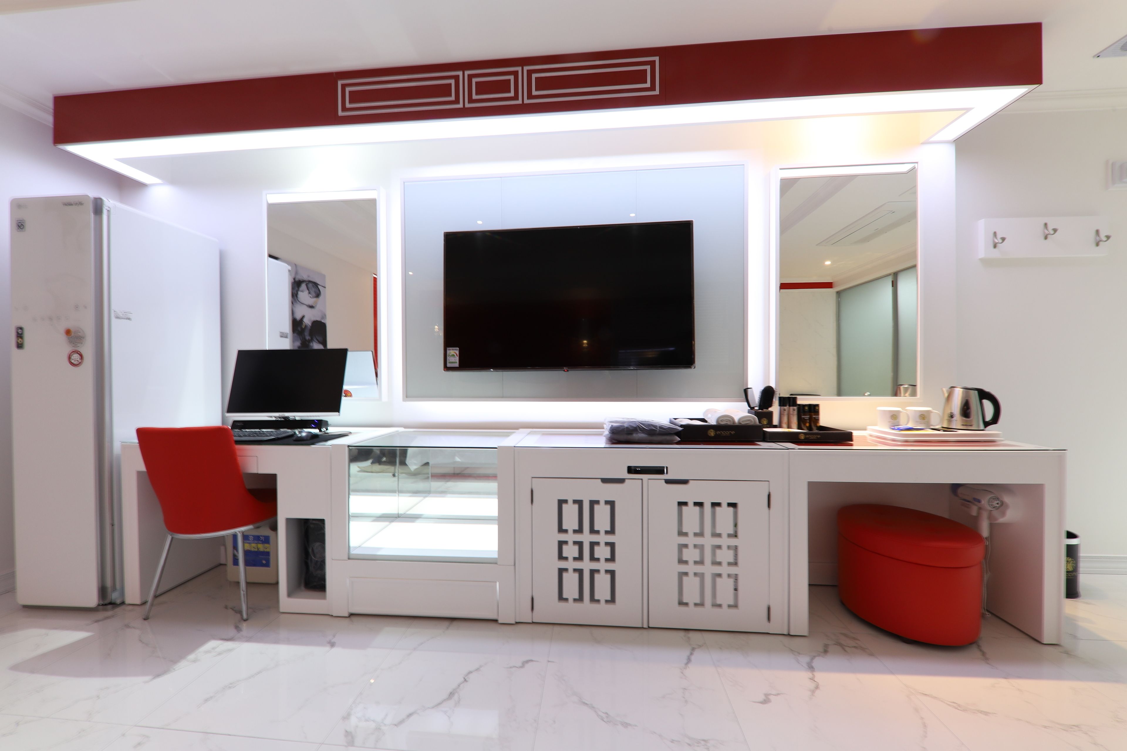 Une pièce moderne et bien éclairée, avec un bureau, une chaise rouge, un téléviseur et un pouf rouge.