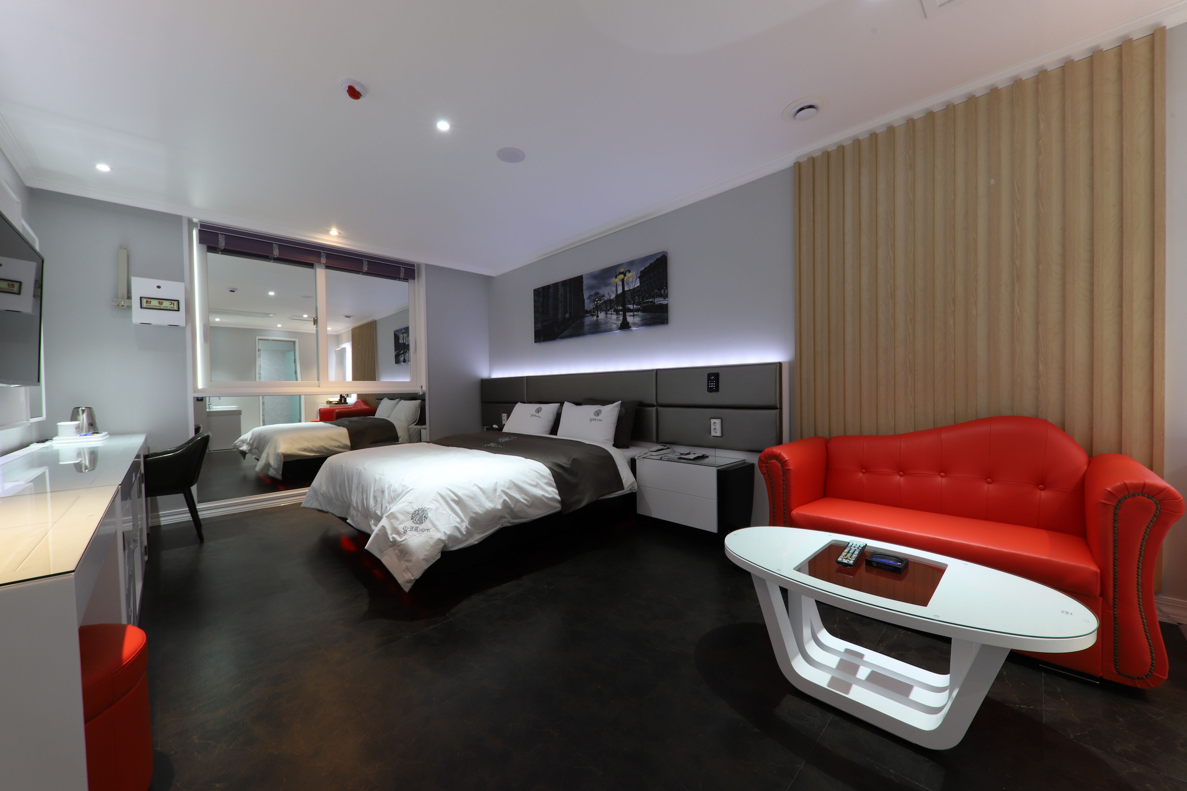 Una camera d'albergo moderna con un letto, un divano rosso, un tavolino bianco e una scrivania con una sedia.