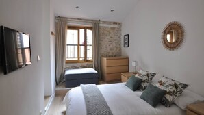 A bedroom with a bed, a dresser, a mirror, and a window with curtains. - Spacious new one-bedroom apartment in the heart of the Old Town (Antibes)