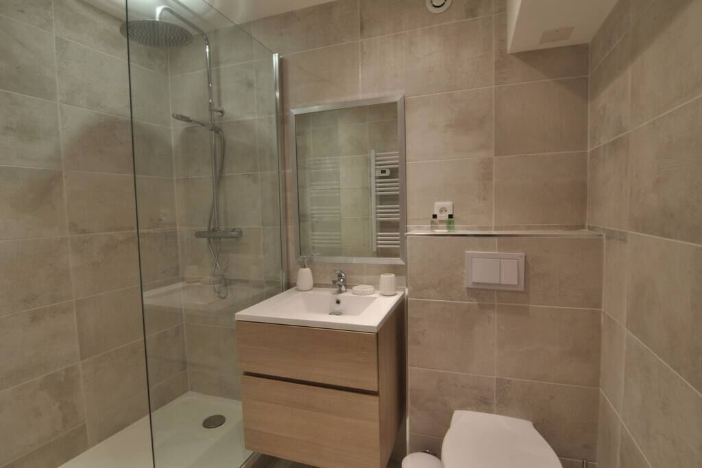 Un baño moderno con ducha envuelta en vidrio, tocador de madera con lavamanos y un inodoro.