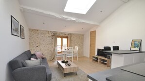 A modern living room with a grey sofa, a wooden coffee table, and a dining area with white chairs. - Spacious new one-bedroom apartment in the heart of the Old Town (Antibes)