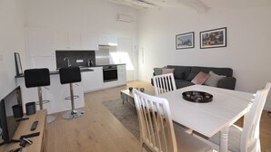 A modern kitchen with white cabinets, a dining area with a white table and chairs, and a grey sofa. - Spacious new one-bedroom apartment in the heart of the Old Town (Antibes)