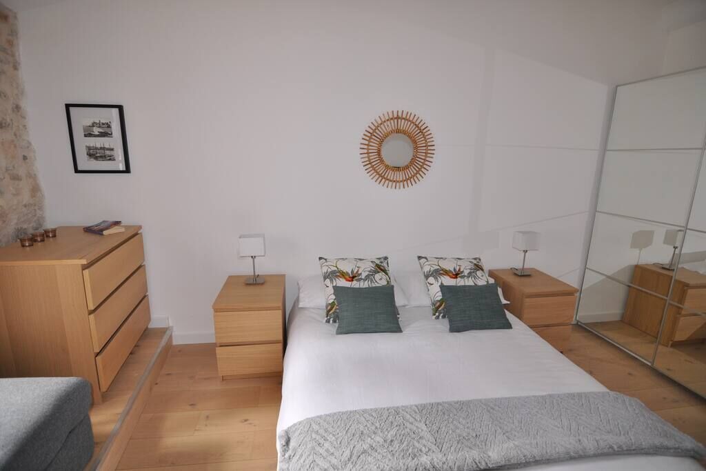 Quarto com cama, duas mesas de cabeceira, cômoda, espelho e um quadro na parede.