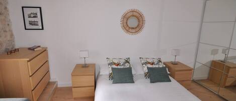 Quarto com cama, duas mesas de cabeceira, cômoda, espelho e um quadro na parede.