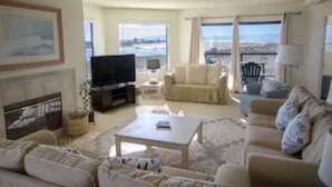 A spacious living room with a large television, comfortable seating, and a view of the sea. - Panoramic views, 2-person soaking tub, Fireplace 2nd Floor (Moss Landing)