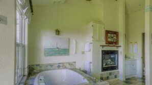 A bathroom with a bathtub, a sink, and a mirror. There is a window with a view of the sea. - Panoramic views, 2-person soaking tub, Fireplace 2nd Floor (Moss Landing)