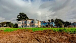 A multi-story residential building with a flat roof and large windows, surrounded by greenery and under a cloudy sky. - Panoramic views, 2-person soaking tub, Fireplace 2nd Floor (Moss Landing)
