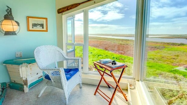 A room with a large window, a wicker chair, a small table, and a dresser. - Panoramic views, 2-person soaking tub, Fireplace 2nd Floor (Moss Landing)