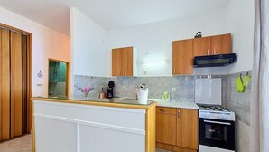 A compact kitchen with wooden cabinets, a white countertop, a stove, and a refrigerator. - Holiday house Selak * large garden, terrace, sea view, free WiFi (Tucepi)