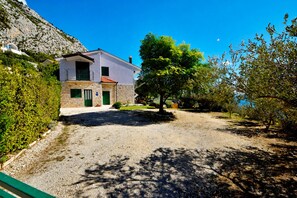 A two-story building with a stone facade, a paved driveway, and a tree in the foreground. - Holiday house Selak * large garden, terrace, sea view, free WiFi (Tucepi)