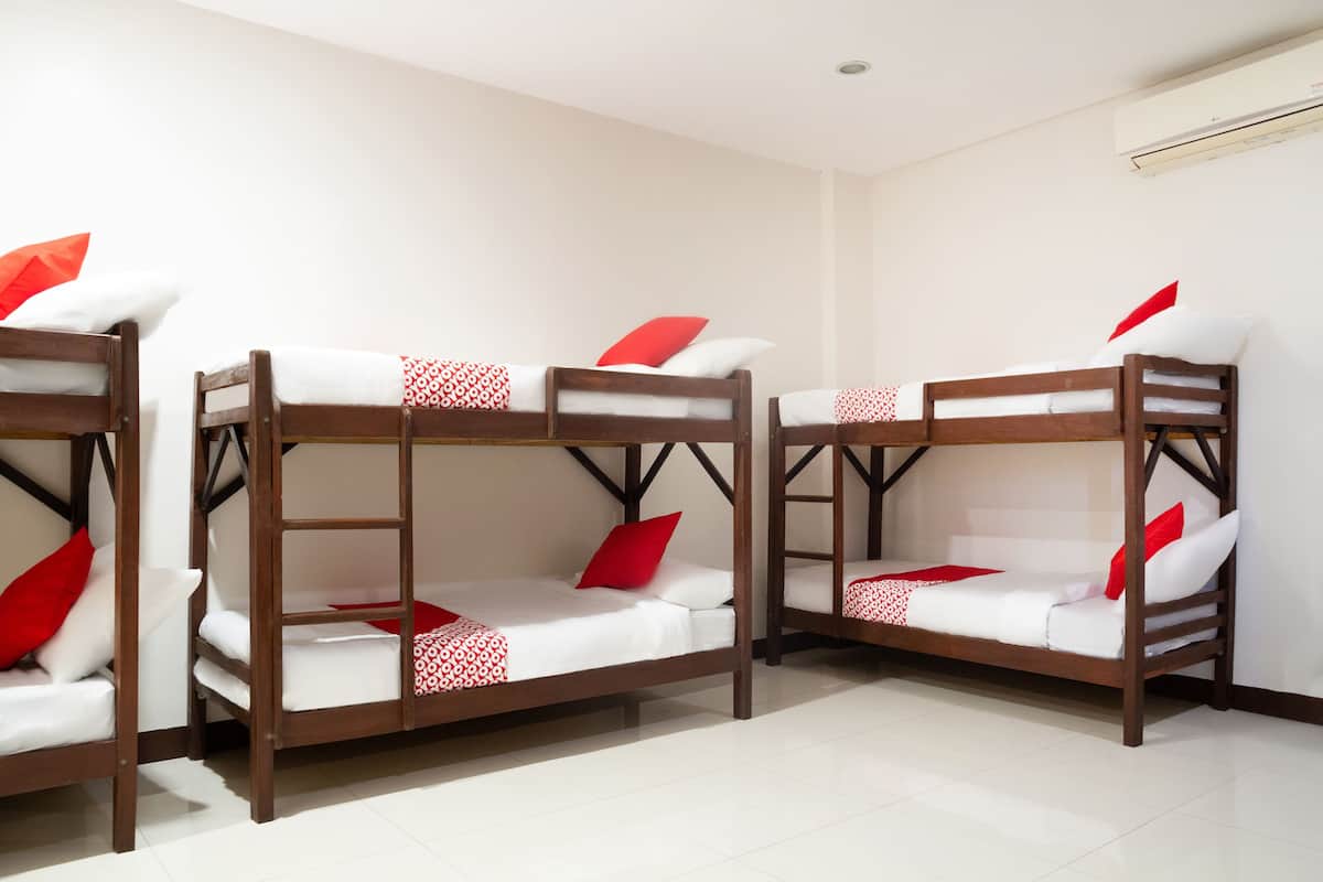 Three bunk beds with white bedding and red pillows in a room with white walls and a tiled floor.