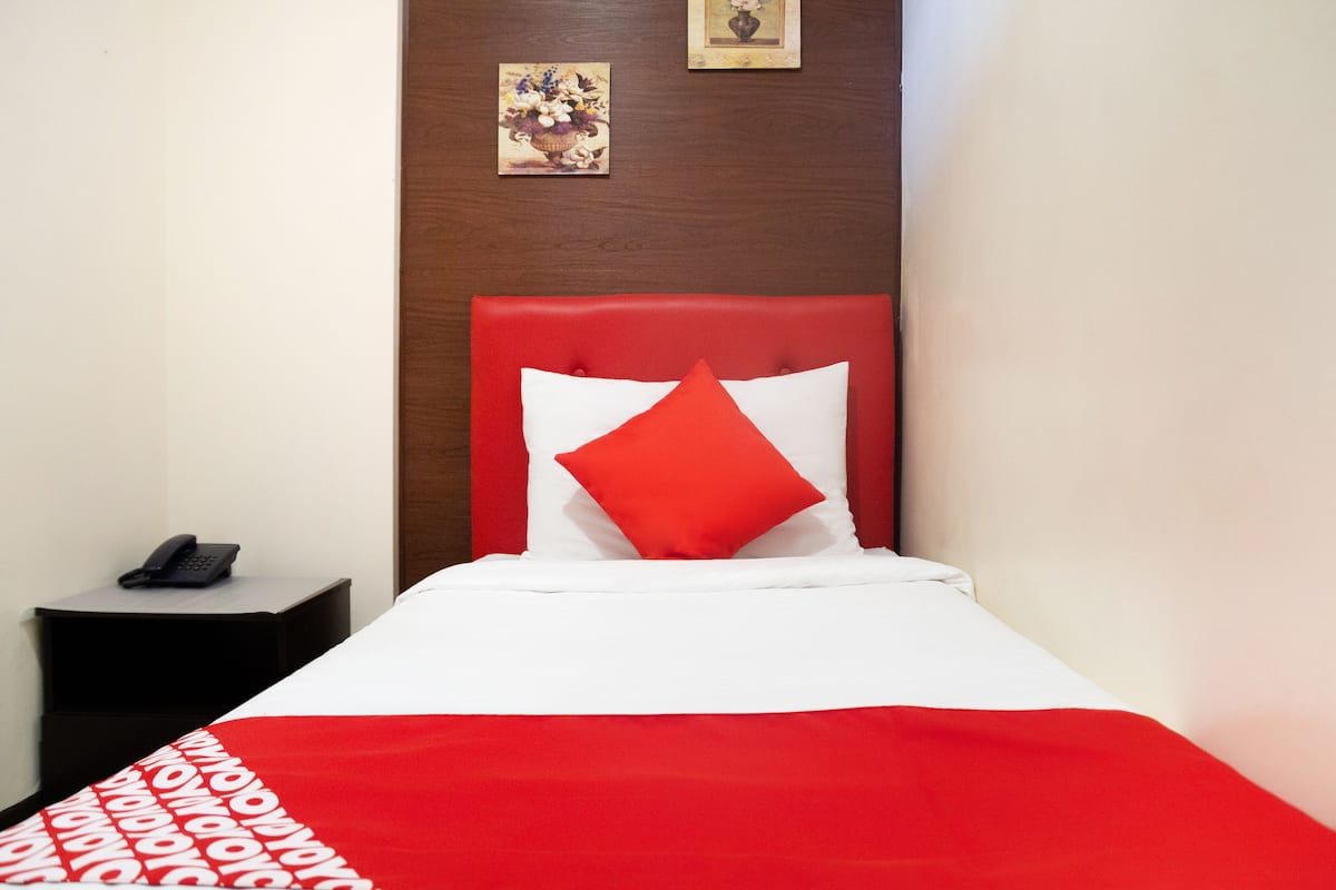 A hotel room with a red and white bedspread, a red headboard, and a small bedside table with a phone.