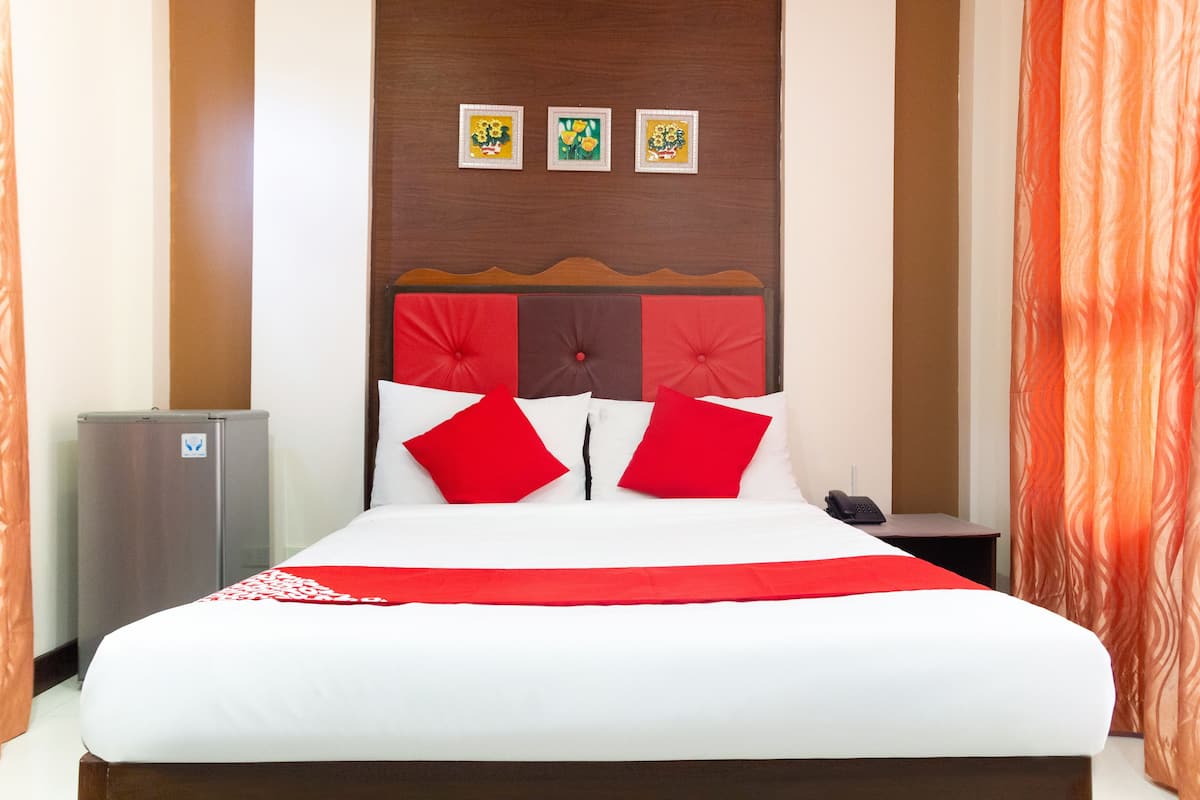 A hotel room with a bed, a nightstand, a refrigerator, and a wall with three framed pictures.