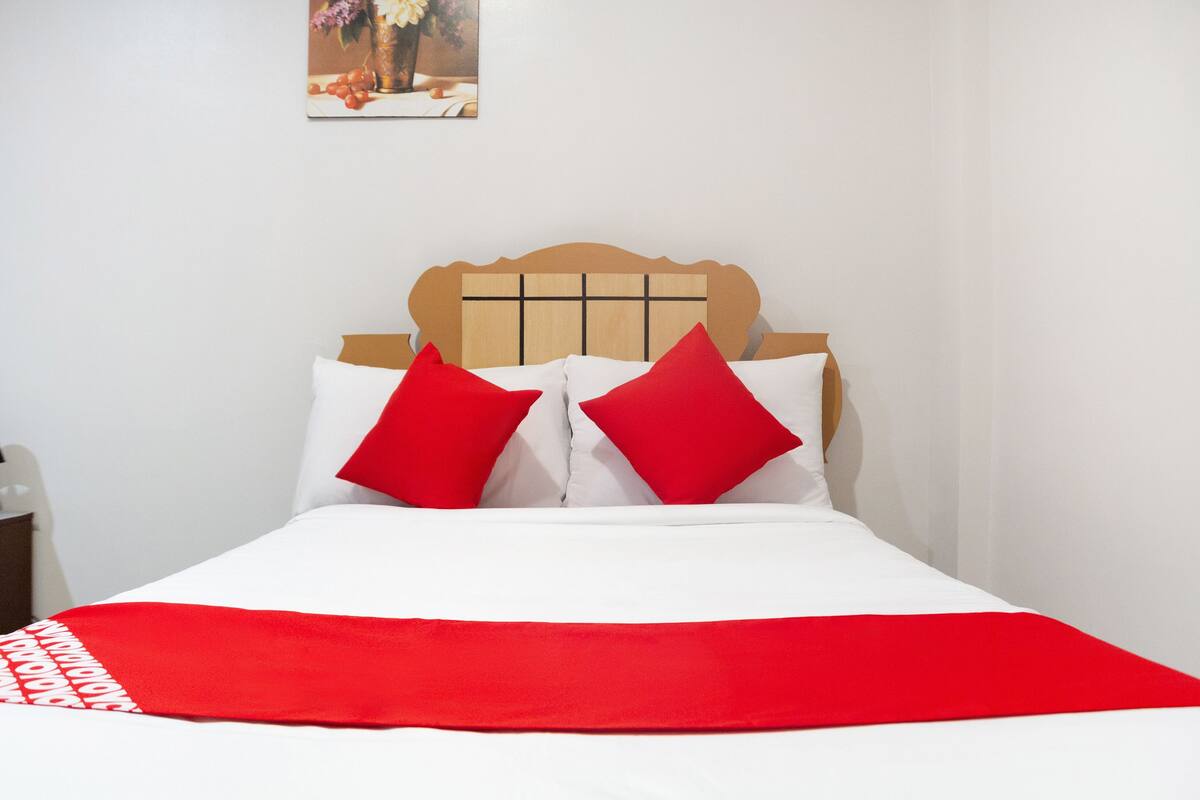 A bed with a wooden headboard, white bedding, and red accents.