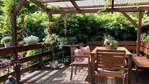 Un terrazzo in legno con una pergola, arredi da esterno e vasi con piante.