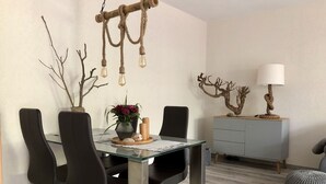 Un'area pranzo con tavolo in vetro, sedie nere, un vaso con fiori e un rustico lampadario in corda.