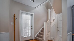 Eine Treppe führt zu einer zweiten Etage, mit Holzdielen, einer weißen Tür mit Fenster und einer Deckenleuchte.
