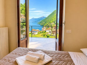 Une chambre Ă coucher avec un lit, une fenĂȘtre donnant sur une montagne et un lac, et un balcon avec une balustrade.